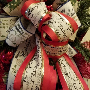 Puede incluir: Un lazo de corona navide&ntilde;a con cinta roja y blanca. La cinta tiene un borde dorado y el texto "Feliz Navidad" impreso en ella.