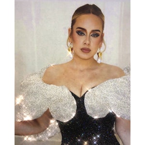 May include: A woman wearing a black sequined dress with large silver glitter puff sleeves. She has blonde hair and is wearing gold earrings.