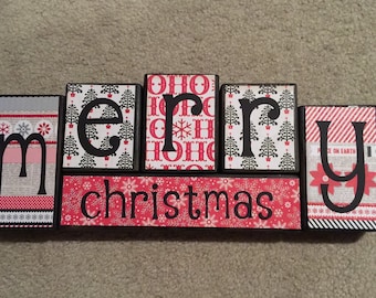 May include: Red and black wooden blocks spelling out "merry christmas" with various holiday patterns on each block.