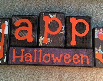 May include: Wooden blocks spelling "Happy Halloween" with orange letters and various Disney character designs on each block.
