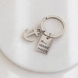 May include: Silver keyring with an anchor charm and a rectangular tag that reads "Moin Heimat Hafen".