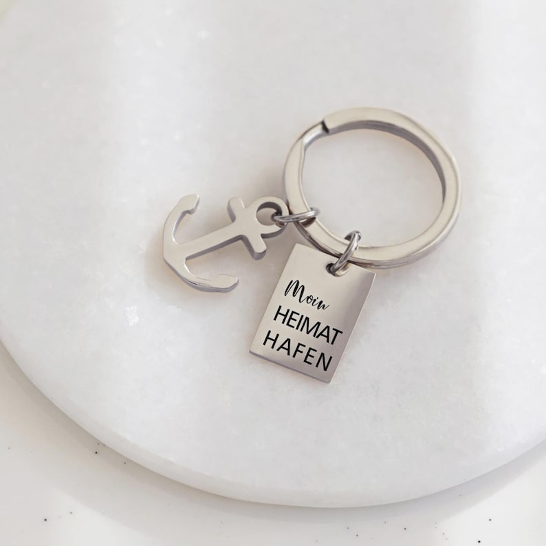 May include: Silver keyring with an anchor charm and a rectangular tag that reads "Moin Heimat Hafen".