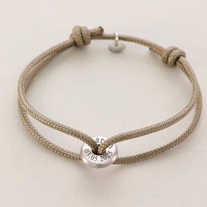 May include: A beige rope bracelet with a silver charm that says "03.05.2025" on it.