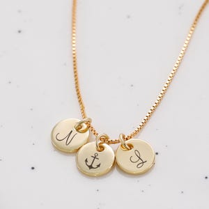 Op de afbeelding: Gouden ketting met drie bedels: een letter N, een anker en een letter J.