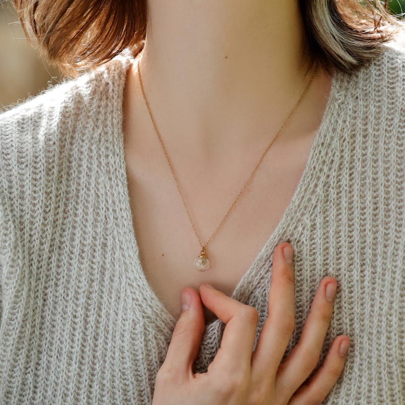 May include: A gold chain necklace with a small glass pendant containing a dried flower.