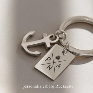 May include: Silver keyring with an anchor charm and a rectangular tag engraved with the letters "PNA" and a paw print. The tag has the text "personalisierbare R&uuml;ckseite" on the back.