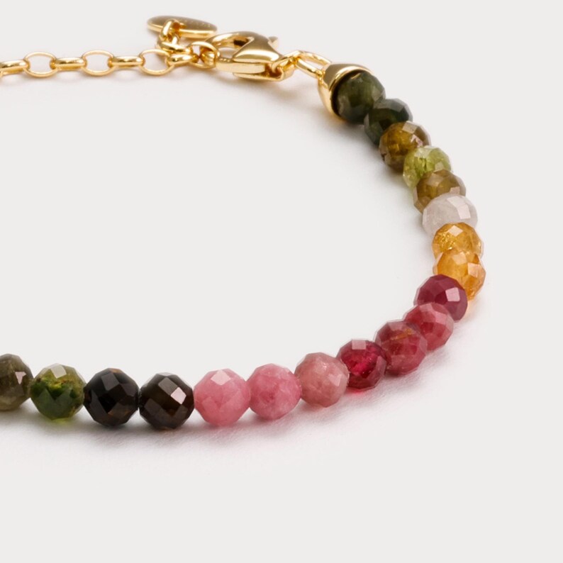 May include: A gold chain bracelet with a clasp and a row of faceted gemstone beads in shades of green, pink, and red.