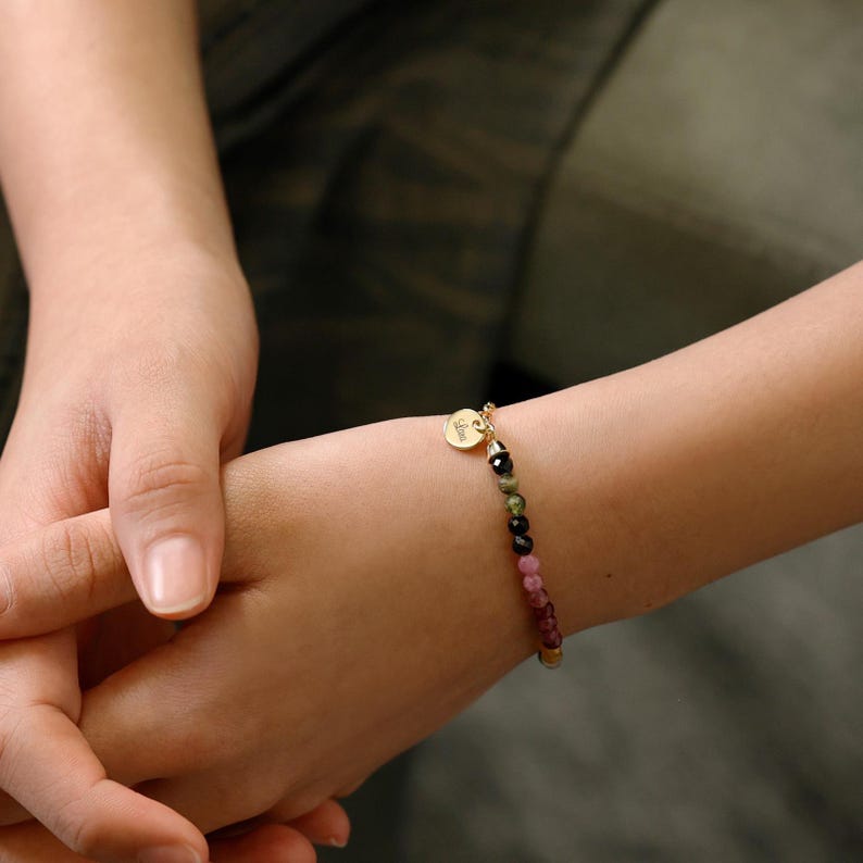 May include: A gold bracelet with a small round charm that says "Love" and a beaded chain with pink, green, and black beads.
