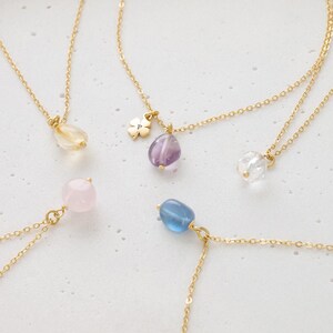 May include: A collection of gold-toned necklaces, each featuring a different gemstone pendant. The pendants include a clear quartz, amethyst, rose quartz, blue gemstone, and a yellow gemstone. One necklace has a four-leaf clover charm.