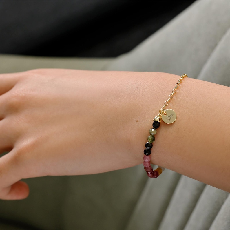 May include: A gold chain bracelet with a round charm that says "Love" and a multi-coloured beaded section. The beads are pink, green, and black.