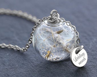 Op de afbeelding: Een zilveren ketting met een glazen bolhanger gevuld met witte paardenbloemzaden en kleine gouden glitterdeeltjes. Een kleine, ronde zilveren bedel hangt aan de bovenkant, gegraveerd met de Duitse tekst "Lieblings mensch".