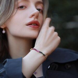 May include: A gold chain bracelet with a row of colourful gemstone beads. The beads are pink, green, yellow, and black.