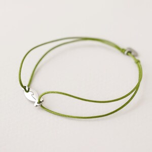 May include: A green string bracelet with a silver charm shaped like a wave.