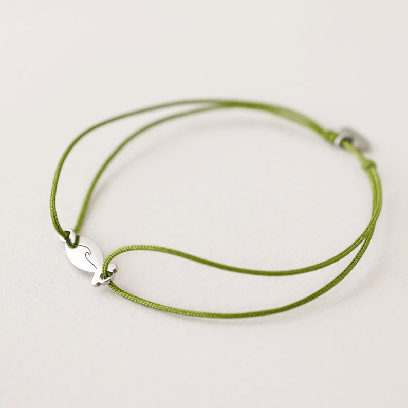 May include: A green string bracelet with a silver charm shaped like a wave.