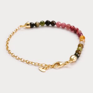 May include: A gold chain bracelet with a heart charm and a multi-coloured gemstone bead strand. The beads are green, black, pink, and yellow.