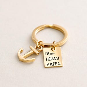 May include: Gold-toned keychain with an anchor charm and a square tag that reads "Moin Heimat Hafen".