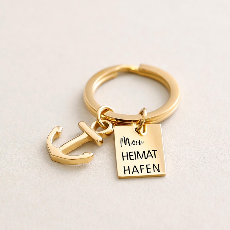 May include: Gold-toned keychain with an anchor charm and a square tag that reads "Moin Heimat Hafen".