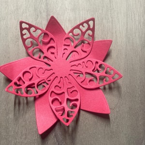 May include: A pink paper flower with a delicate, intricate design. The flower has multiple layers and is cut out in a floral pattern.