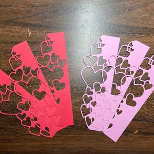 May include: Four pink and four red paper strips with a heart cut-out design. The strips are arranged in a fan shape.