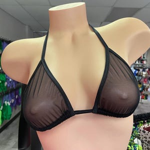 May include: A black sheer bikini top displayed on a mannequin. The triangle cups are connected by a halter neck strap and a thin band that goes around the back. The material is a see-through mesh.