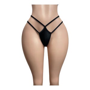 May include: A black thong featuring a minimalist design with thin, elasticized straps that cross over the front hip area. The garment is constructed from a smooth, solid black fabric, creating a sleek and simple aesthetic for this piece of intimate apparel.