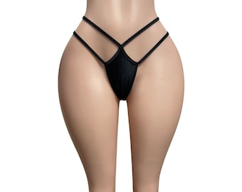 May include: A black thong featuring a minimalist design with thin, elasticized straps that cross over the front hip area. The garment is constructed from a smooth, solid black fabric, creating a sleek and simple aesthetic for this piece of intimate apparel.