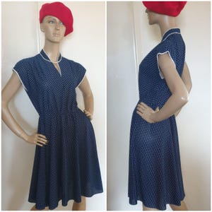 May include: A navy blue dress with a white polka dot pattern, featuring short sleeves, a V-neckline with white trim, and a flared skirt. The dress is displayed on a mannequin wearing a bright red beret, shown from both front and side angles.