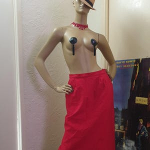May include: A red skirt with a high waist and a straight silhouette. The skirt is knee-length and has a simple design.