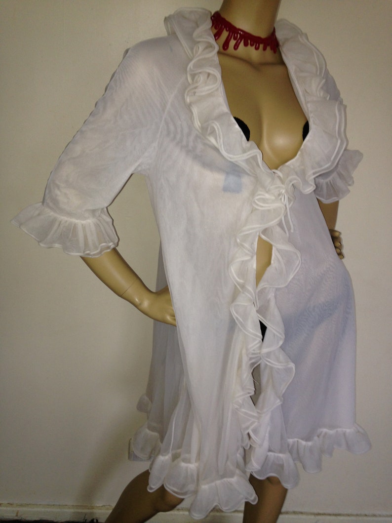 May include: White sheer robe with ruffled trim and a tie closure. The robe has a deep V-neckline and three-quarter sleeves.