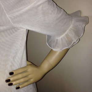 May include: White sheer blouse with a ruffled sleeve detail. The blouse is made of a lightweight fabric and has a relaxed fit.