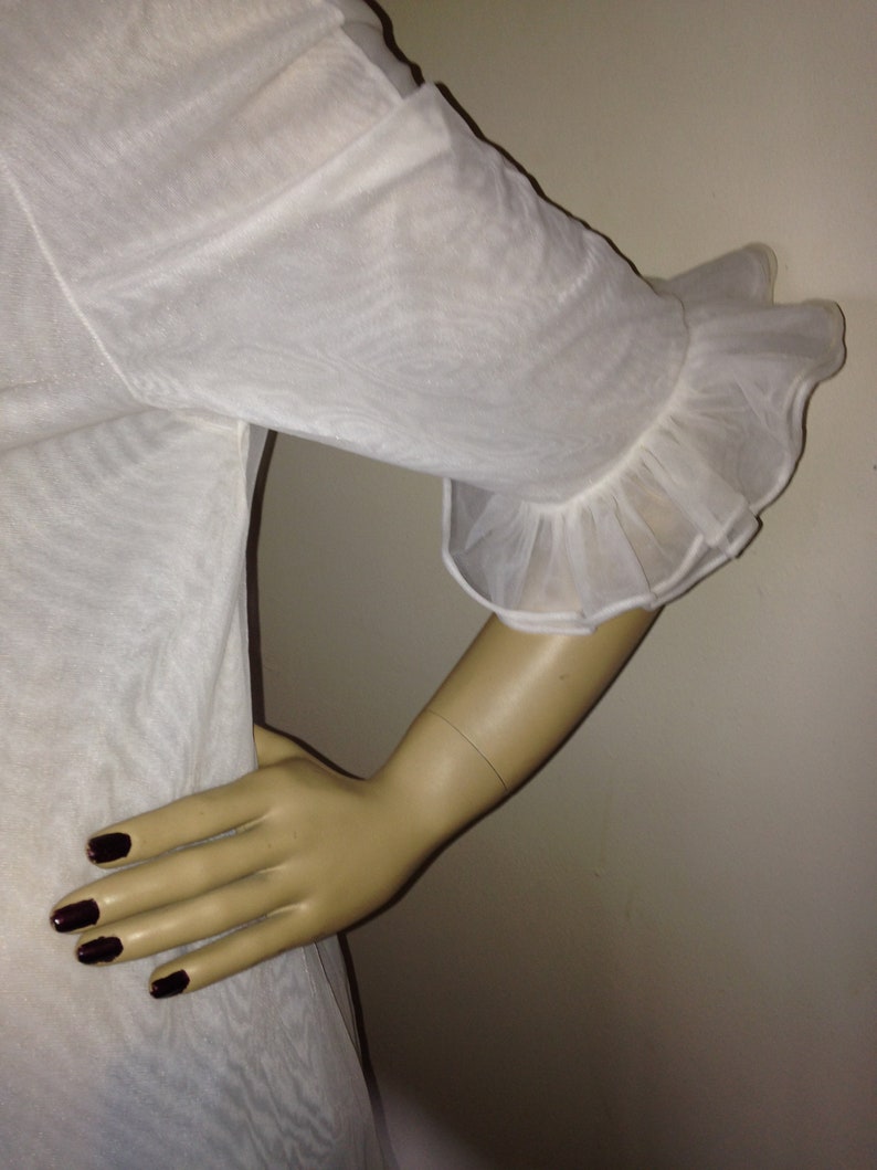 May include: White sheer blouse with a ruffled sleeve detail. The blouse is made of a lightweight fabric and has a relaxed fit.