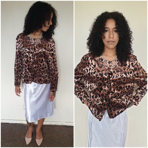 May include: A woman is wearing a brown and black leopard print satin blouse with a white satin skirt. She is wearing a silver necklace.