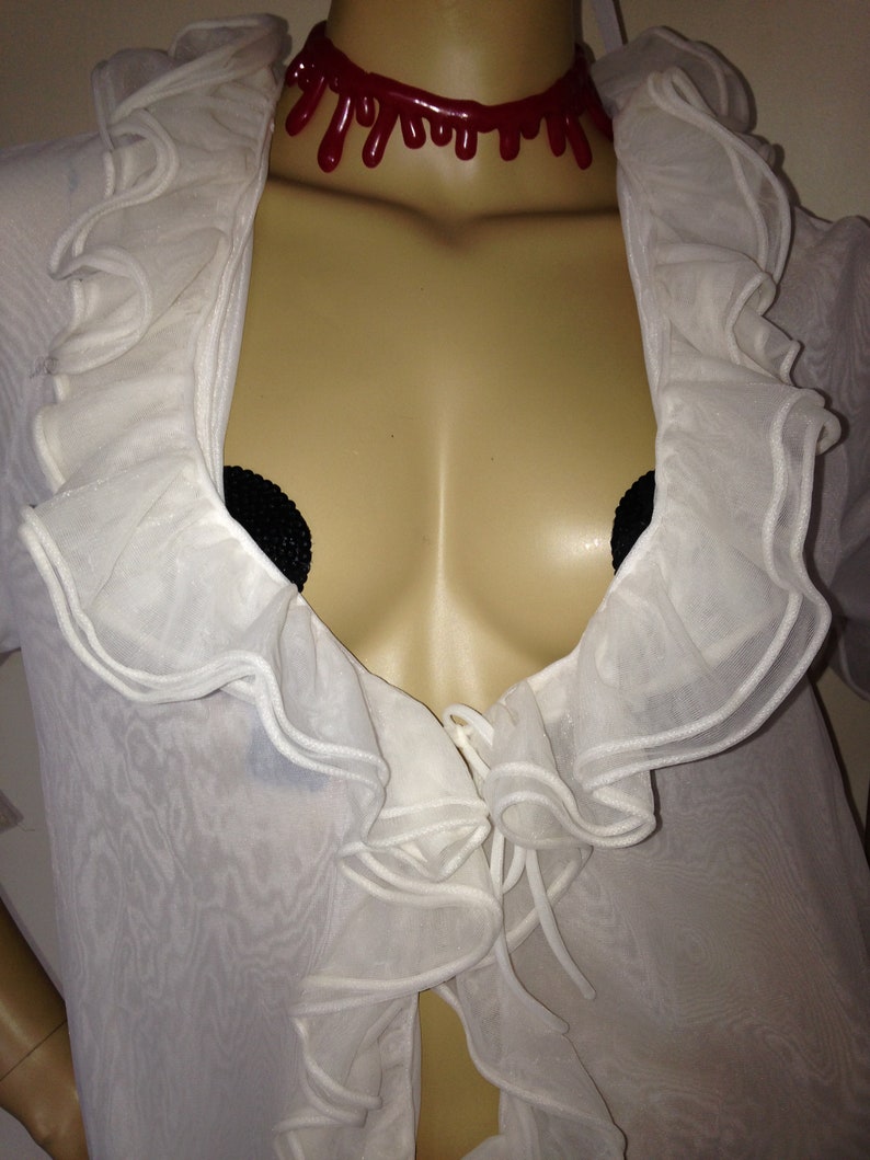 May include: A white sheer top with ruffled trim and a red dripping blood-like choker necklace.