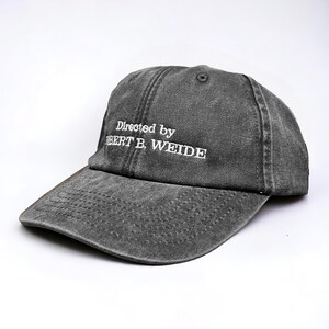 May include: A gray, distressed, cotton baseball cap with white embroidery that reads "Directed by Robert B. Weide".