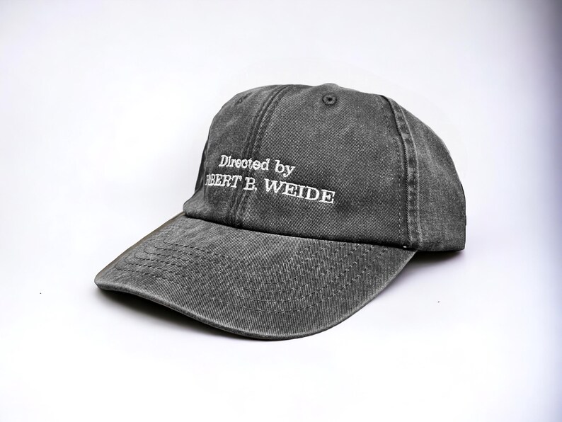 May include: A gray, distressed, cotton baseball cap with white embroidery that reads "Directed by Robert B. Weide".