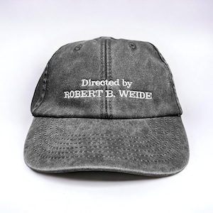 May include: A black distressed baseball cap with white embroidered text that reads "Directed by ROBERT B. WEIDE".