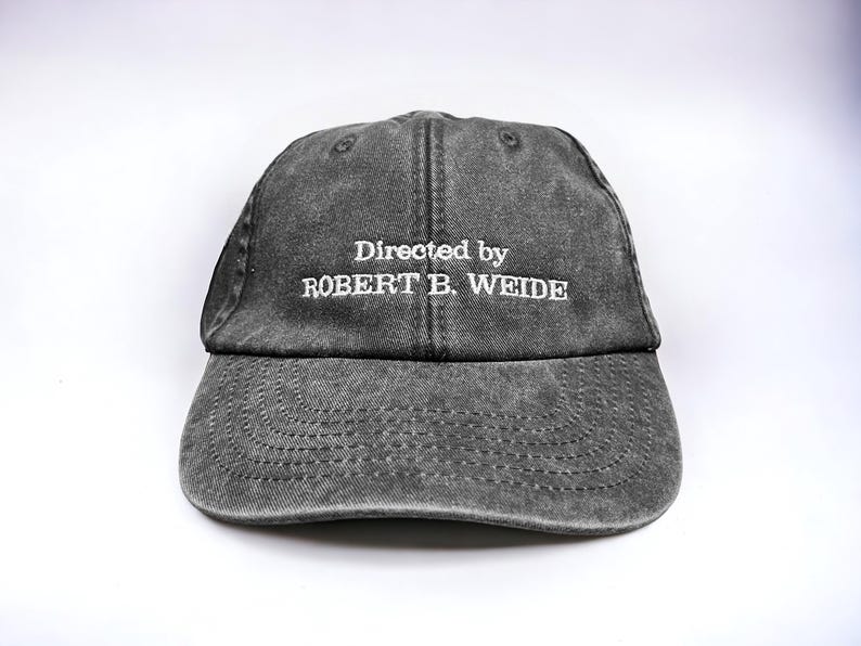May include: A black distressed baseball cap with white embroidered text that reads "Directed by ROBERT B. WEIDE".