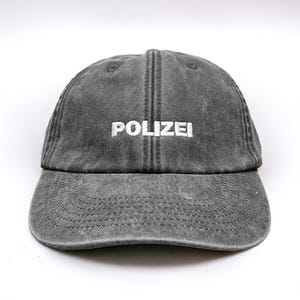May include: A dark grey denim baseball cap with the word "POLIZEI" embroidered in white on the front.