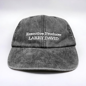 May include: A black denim baseball cap with white embroidered text that reads "Executive Producer LARRY DAVID".