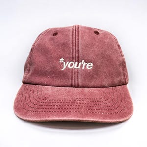 May include: A maroon baseball cap with a white embroidered star and the text "you're" on the front.