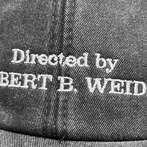 May include: A black baseball cap with white embroidered text that reads "Directed by ROBERT B. WEIDE".