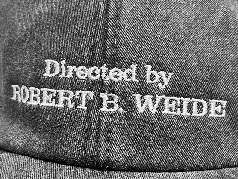 May include: A black baseball cap with white embroidered text that reads "Directed by ROBERT B. WEIDE".