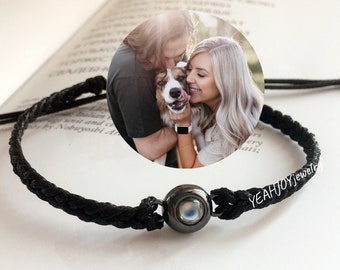 May include: A black braided cord bracelet with a black bead featuring a moonstone and a photo of a couple and their dog.