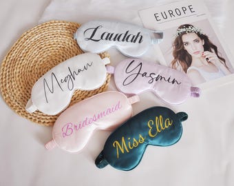 Puede incluir: Cinco antifaces de satén en blanco, rosa y verde azulado, cada uno bordado con un nombre en un color contrastante. Los nombres son "Laudah", "Meghan", "Yasmin", "Bridesmaid" y "Miss Ella". Los antifaces están sobre una estera tejida.
