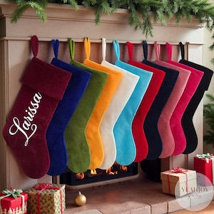 Op de afbeelding: Een rij van tien kerstsokken van fluweel in diverse kleuren, waaronder bordeaux, blauw, groen, geel, wit, lichtblauw, rood, marineblauw, roze en zwart. De bordeauxrode sok is voorzien van de witte cursieve naam Larissa op de boord.
