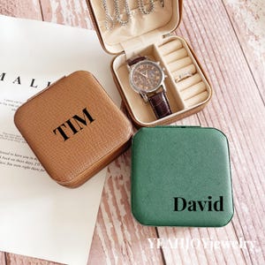 May include: Two personalized square-shaped jewelry boxes. One is brown with the name "TIM" on it. The other is green with the name "David" on it.