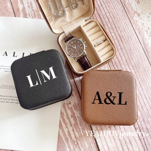 May include: Two small square jewelry boxes with personalized initials. The black box has the initials "L/M" and the brown box has the initials "A&L".