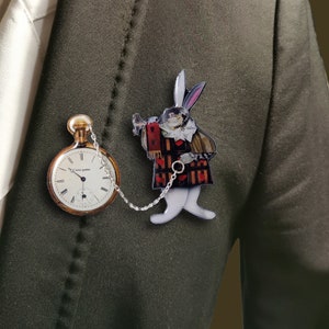 May include: A white rabbit wearing a waistcoat and holding a pocket watch, with a chain attached to a pocket watch with roman numerals, on a dark green background.