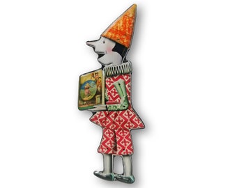 May include: A whimsical, hand-painted wooden figurine of a jester holding a book with the letters "ABC" on the cover. The jester is wearing a red and white patterned costume with a green collar and a tall orange hat.