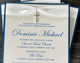 May include: Elegant First Holy Communion invitations. The invitations feature a white card with navy blue borders, a white ribbon, and a silver cross charm. The text reads "Dominic Michael" and event details.